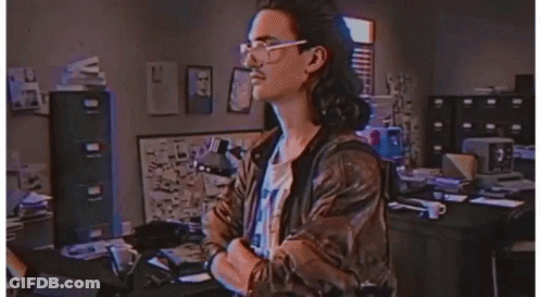 A Man Wearing Glasses And A Leather Jacket Stands In Front Of A Sign That Says Hackerman GIF