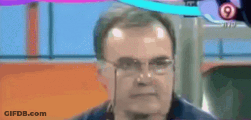 A Man Wearing Glasses And A Medal Around His Neck Is Talking On A Tv Screen . GIF