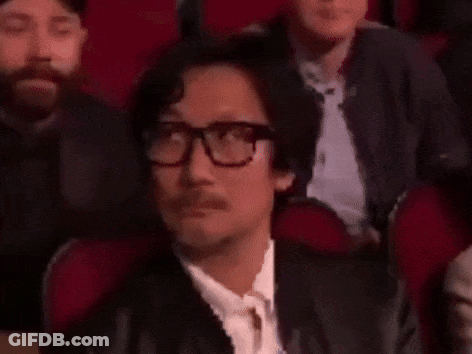 A Man Wearing Glasses And A Mustache Is Sitting In A Theatre . GIF