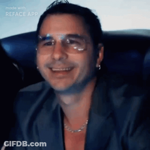 A Man Wearing Glasses And A Necklace Is Smiling In A Video Made With Reface App GIF