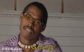 A Man Wearing Glasses And A Necklace Is Smiling With The Words `` Sa Da Tay '' Behind Him . GIF
