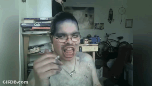 A Man Wearing Glasses And A Necklace With The Letter G On It Is Smoking GIF