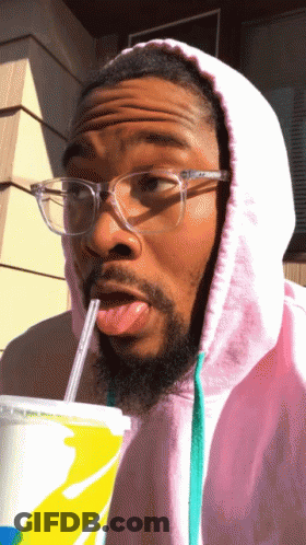 A Man Wearing Glasses And A Pink Hoodie Drinks From A Cup With A Straw GIF