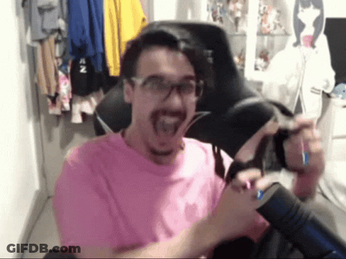 A Man Wearing Glasses And A Pink Shirt Is Sitting In A Chair With His Mouth Open GIF
