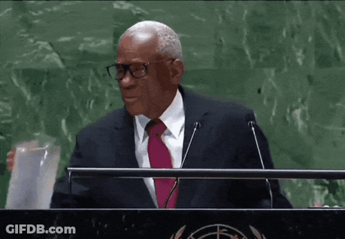 A Man Wearing Glasses And A Pink Tie Stands At A Podium GIF