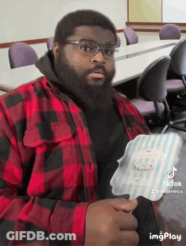A Man Wearing Glasses And A Plaid Shirt Is Holding A Piece Of Paper With A Ring On It .. GIF