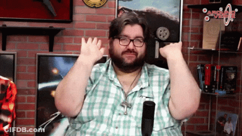 A Man Wearing Glasses And A Plaid Shirt Is Sitting In Front Of A Brick Wall With A Sign That Says Around The World GIF
