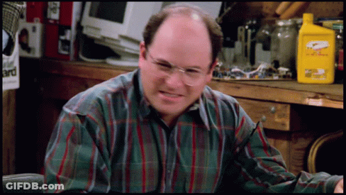 A Man Wearing Glasses And A Plaid Shirt Is Sitting In Front Of A Table With A Yellow Bottle That Says Eagle One GIF