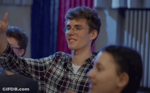 A Man Wearing Glasses And A Plaid Shirt Is Smiling And Raising His Hand In The Air GIF