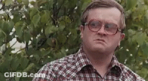 A Man Wearing Glasses And A Plaid Shirt Is Standing In Front Of A Tree And Making A Funny Face . GIF