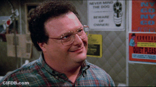 A Man Wearing Glasses And A Plaid Shirt Smiles In Front Of A Sign That Says " Never Mind The Dog " GIF
