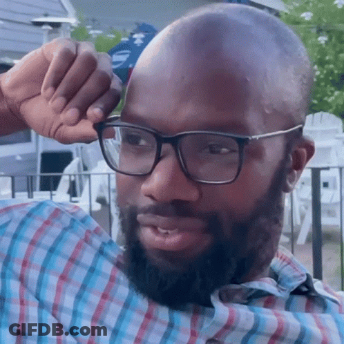 A Man Wearing Glasses And A Plaid Shirt Wipes His Forehead With His Hand GIF