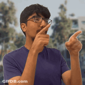 A Man Wearing Glasses And A Purple Shirt Is Pointing At The Camera GIF