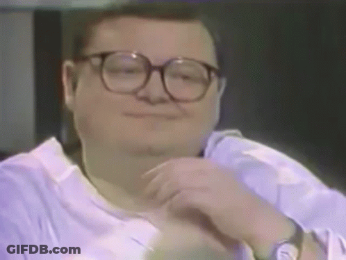 A Man Wearing Glasses And A Purple Shirt Is Smiling And Looking At The Camera . GIF
