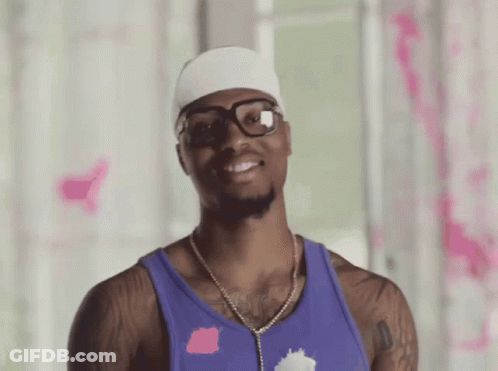 A Man Wearing Glasses And A Purple Tank Top Smiles For The Camera GIF