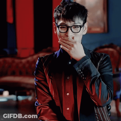 A Man Wearing Glasses And A Red And Black Jacket Is Covering His Mouth With His Hand GIF