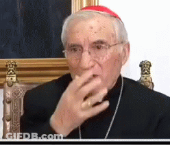A Man Wearing Glasses And A Red Hat Is Sitting In A Chair Covering His Mouth With His Hand . GIF