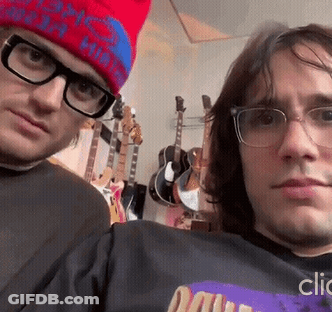 A Man Wearing Glasses And A Red Hat Is Standing Next To Another Man Wearing Glasses And A Hat . GIF