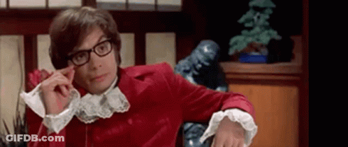 A Man Wearing Glasses And A Red Jacket Is Sitting In A Chair In A Room . GIF