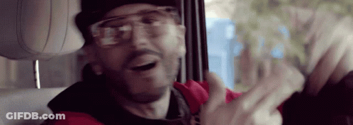 A Man Wearing Glasses And A Red Jacket Is Sitting In The Back Seat Of A Car . GIF