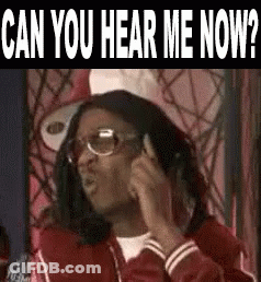 A Man Wearing Glasses And A Red Jacket Is Talking On A Cell Phone And Asking Can You Hear Me Now . GIF