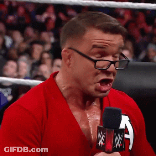 A Man Wearing Glasses And A Red Shirt Is Holding A Microphone And Making A Face . GIF