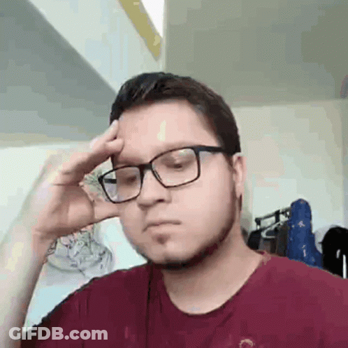 A Man Wearing Glasses And A Red Shirt Is Holding His Hand To His Head . GIF