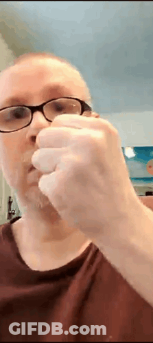 A Man Wearing Glasses And A Red Shirt Is Holding Something In His Hand GIF