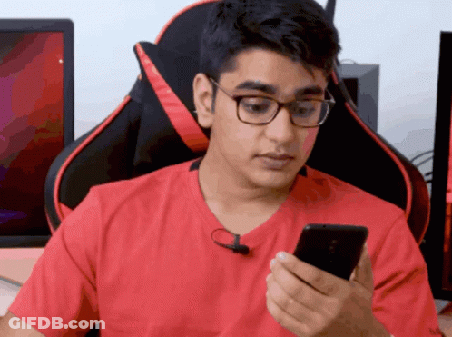 A Man Wearing Glasses And A Red Shirt Is Looking At His Cell Phone GIF