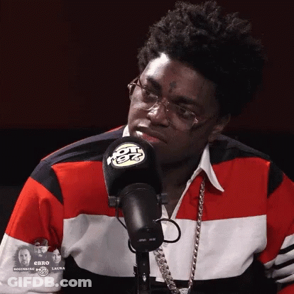 A Man Wearing Glasses And A Red White And Blue Shirt Stands In Front Of A Radio Microphone GIF