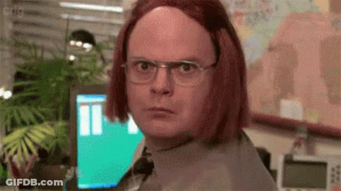 A Man Wearing Glasses And A Red Wig Is Standing In Front Of A Computer Monitor . GIF