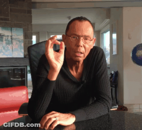 A Man Wearing Glasses And A Ring Sits At A Table With His Hands Folded GIF