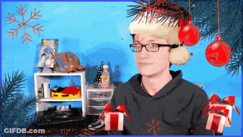 A Man Wearing Glasses And A Santa Hat Stands In Front Of A Christmas Tree GIF
