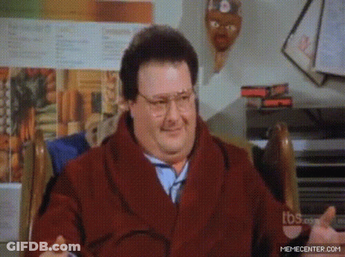 A Man Wearing Glasses And A Scarf Is Sitting In A Chair GIF