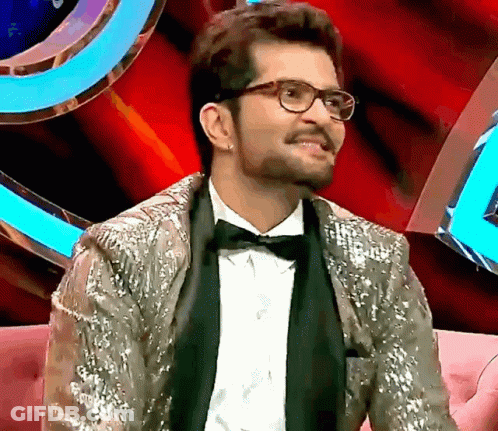 A Man Wearing Glasses And A Sequined Jacket Is Sitting On A Couch GIF