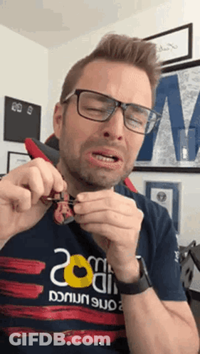 A Man Wearing Glasses And A Shirt That Says 200 On It Is Holding Something In His Hands GIF