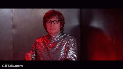 A Man Wearing Glasses And A Silver Shirt Is Pointing At The Camera GIF