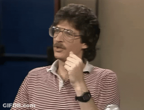 A Man Wearing Glasses And A Striped Shirt Holds His Hand To His Chin GIF