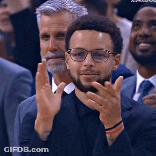 A Man Wearing Glasses And A Suit Is Clapping His Hands In A Crowd Of People . GIF