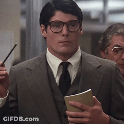 A Man Wearing Glasses And A Suit Is Holding A Notebook GIF
