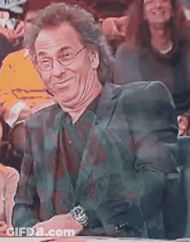 A Man Wearing Glasses And A Suit Is Sitting In A Crowd . GIF