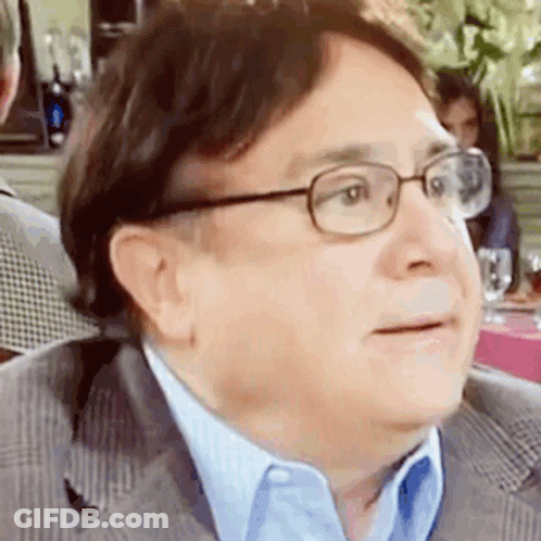 A Man Wearing Glasses And A Suit Is Sitting In A Restaurant . GIF