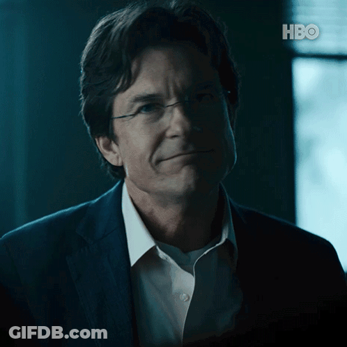 A Man Wearing Glasses And A Suit Is Smiling In Front Of A Hbo Logo GIF
