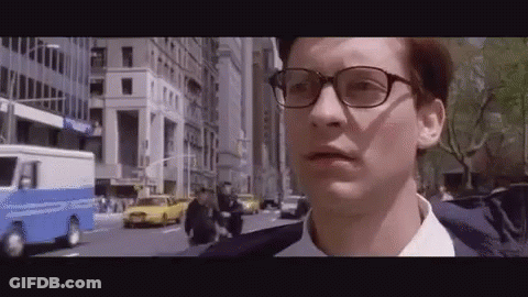 A Man Wearing Glasses And A Suit Is Walking Down A Street . GIF