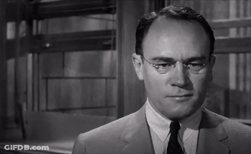 A Man Wearing Glasses And A Suit Looks At The Camera In A Black And White Photo GIF