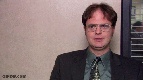A Man Wearing Glasses And A Suit Stands In Front Of A Wall GIF
