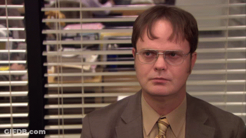 A Man Wearing Glasses And A Suit Stands In Front Of A Window With Blinds GIF