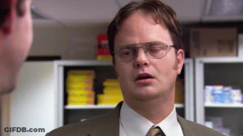 A Man Wearing Glasses And A Suit Talks To Another Man In An Office GIF