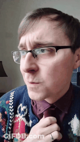 A Man Wearing Glasses And A Sweater Has A Ring On His Left Hand GIF
