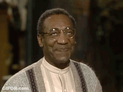 A Man Wearing Glasses And A Sweater Is Smiling And Looking At The Camera . GIF